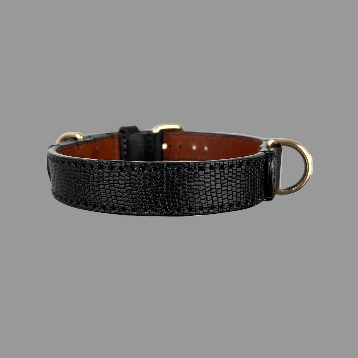 Side detail of a black lizard-embossed leather dog collar showing a gold-tone D-ring secured with reinforced leather and stitching.