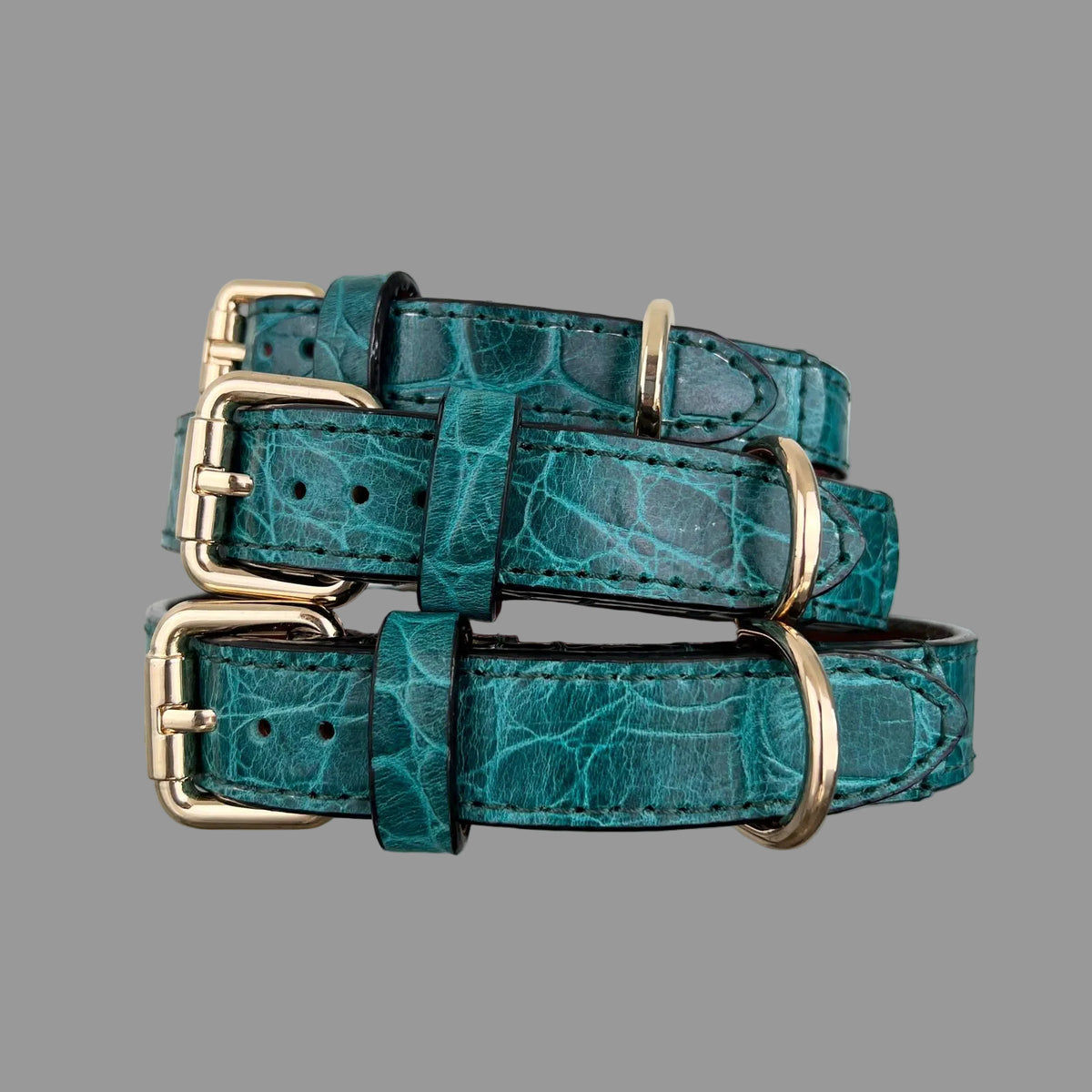 Angled view of three teal embossed leather dog collars showing gold-tone buckles, D-rings and hand-stitched reinforcement.