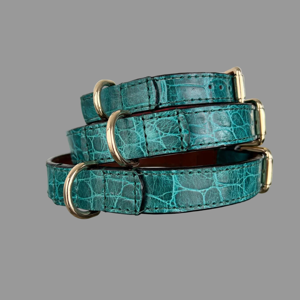 Three stacked teal crocodile-embossed dog collars with matching stitching, black finished edges and gold-tone hardware.