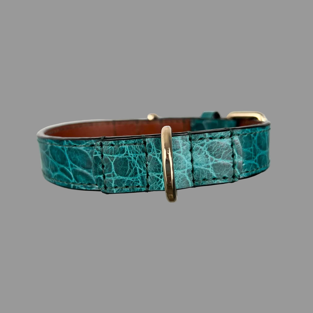 Close view of a gold-tone D-ring secured with reinforced teal embossed leather and hand stitching on a cowhide dog collar.