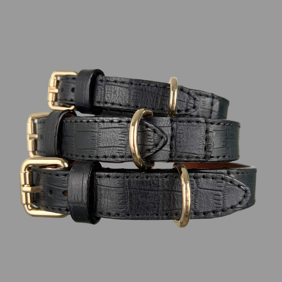 Angled view of three black embossed leather dog collars with gold-tone buckles, D-rings and pointed leather strap ends.