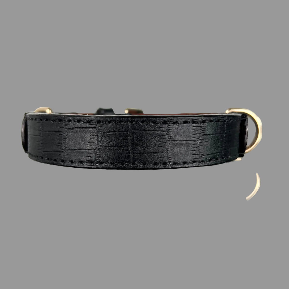 Close-up of rectangular crocodile-style embossing, black stitching and finished edges on a black leather dog collar.