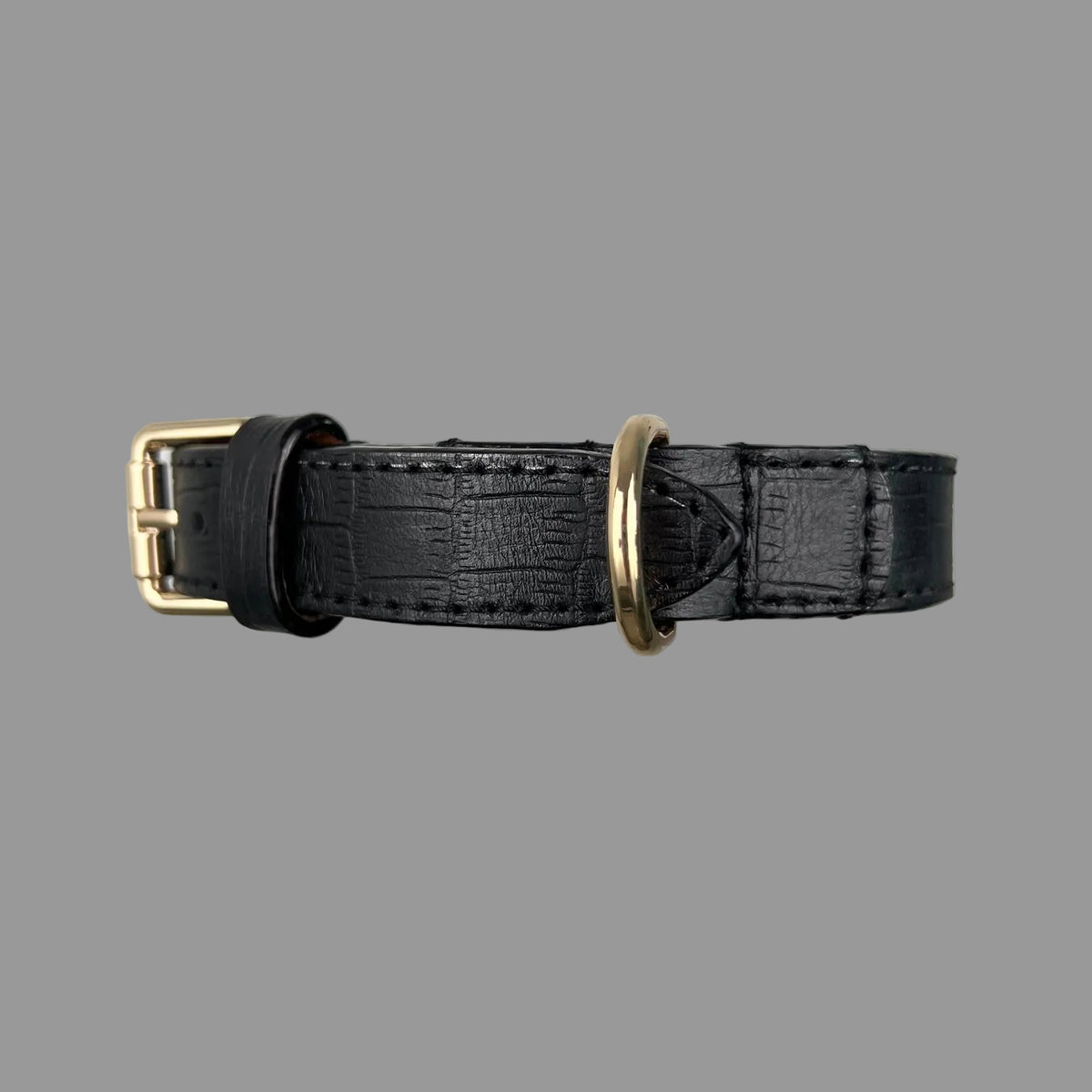 Gold-tone D-ring secured by stitched leather reinforcement beside the buckle and keeper on a black embossed dog collar.