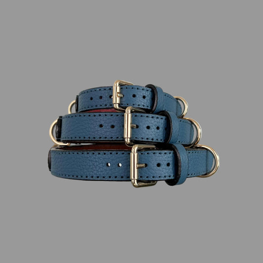 Three denim-blue pebbled leather dog collars stacked to show their widths, gold-tone buckles and matching blue stitching.