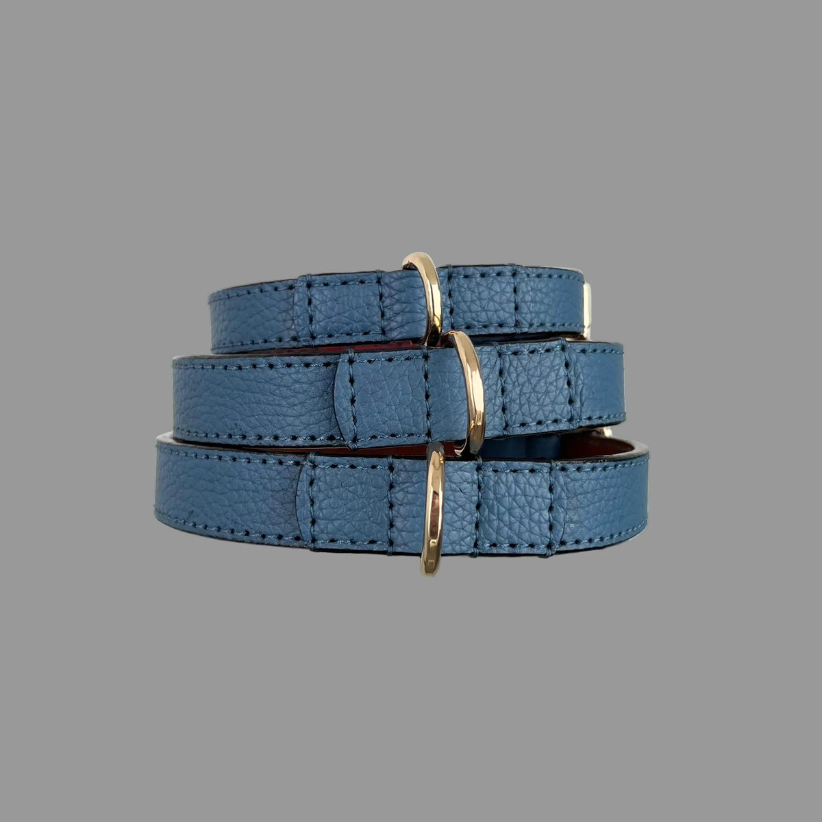 Stacked blue pebbled leather dog collars showing gold-tone D-rings and reinforced, hand-stitched leather attachments.