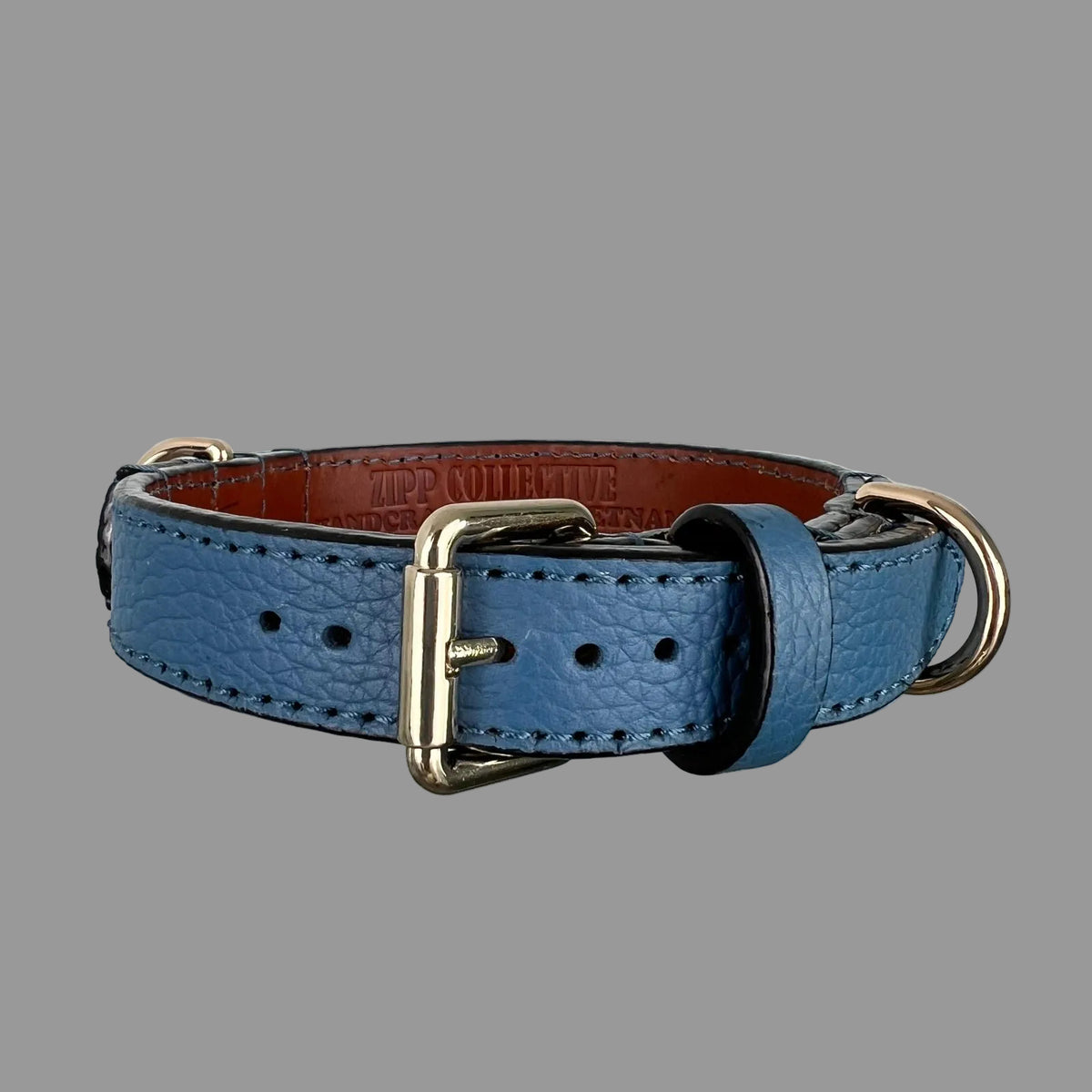 Front view of a denim-blue leather dog collar with a gold-tone buckle, blue keeper and brown lining visible inside.
