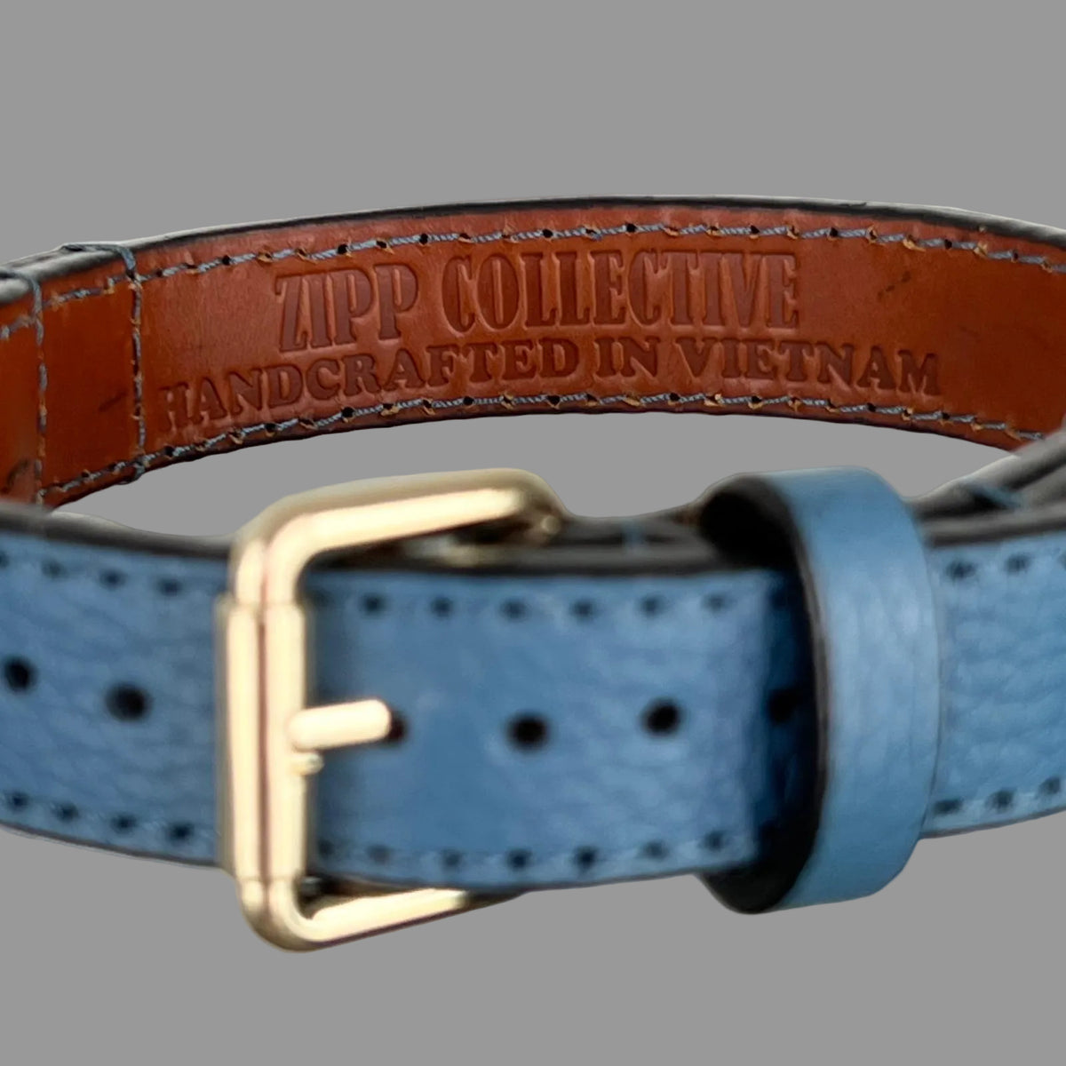 Close-up of the ZIPP COLLECTIVE — HANDCRAFTED IN VIETNAM stamp on the brown lining of a blue leather dog collar.
