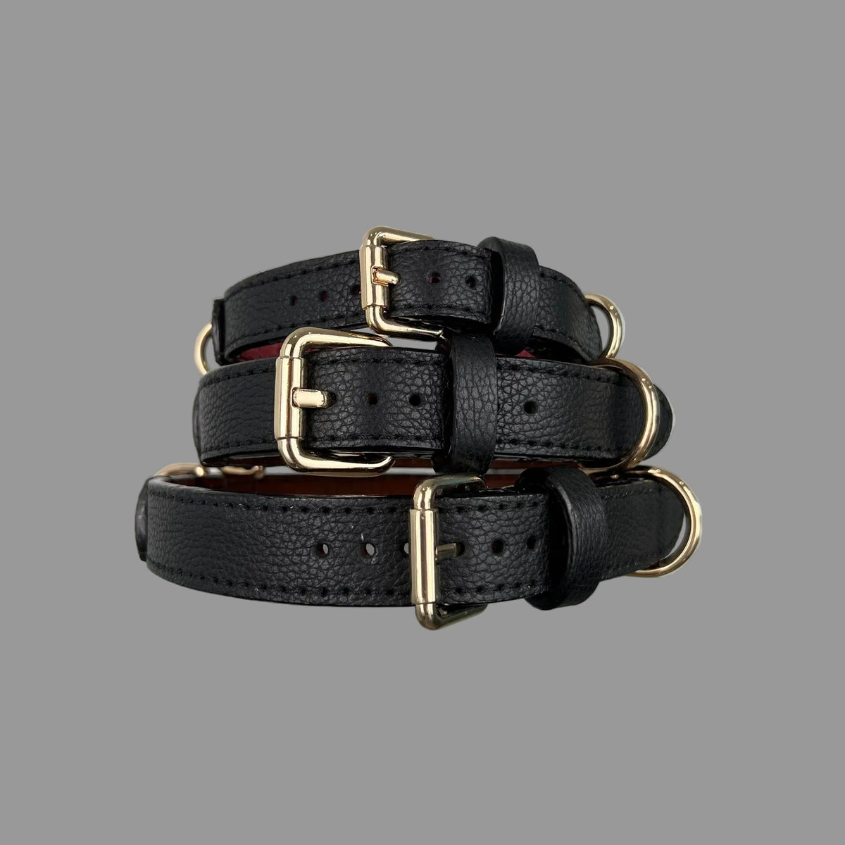 Three black pebbled leather dog collars stacked to show their widths, gold-tone buckles and matching black stitching.