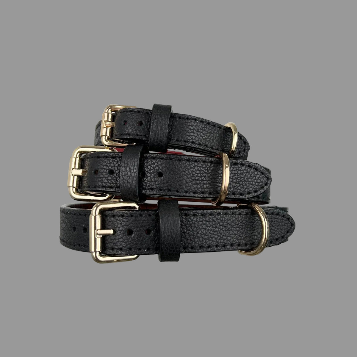 Angled view of three black pebbled dog collars with gold-tone buckles, D-rings, black keeper loops and pointed strap ends.