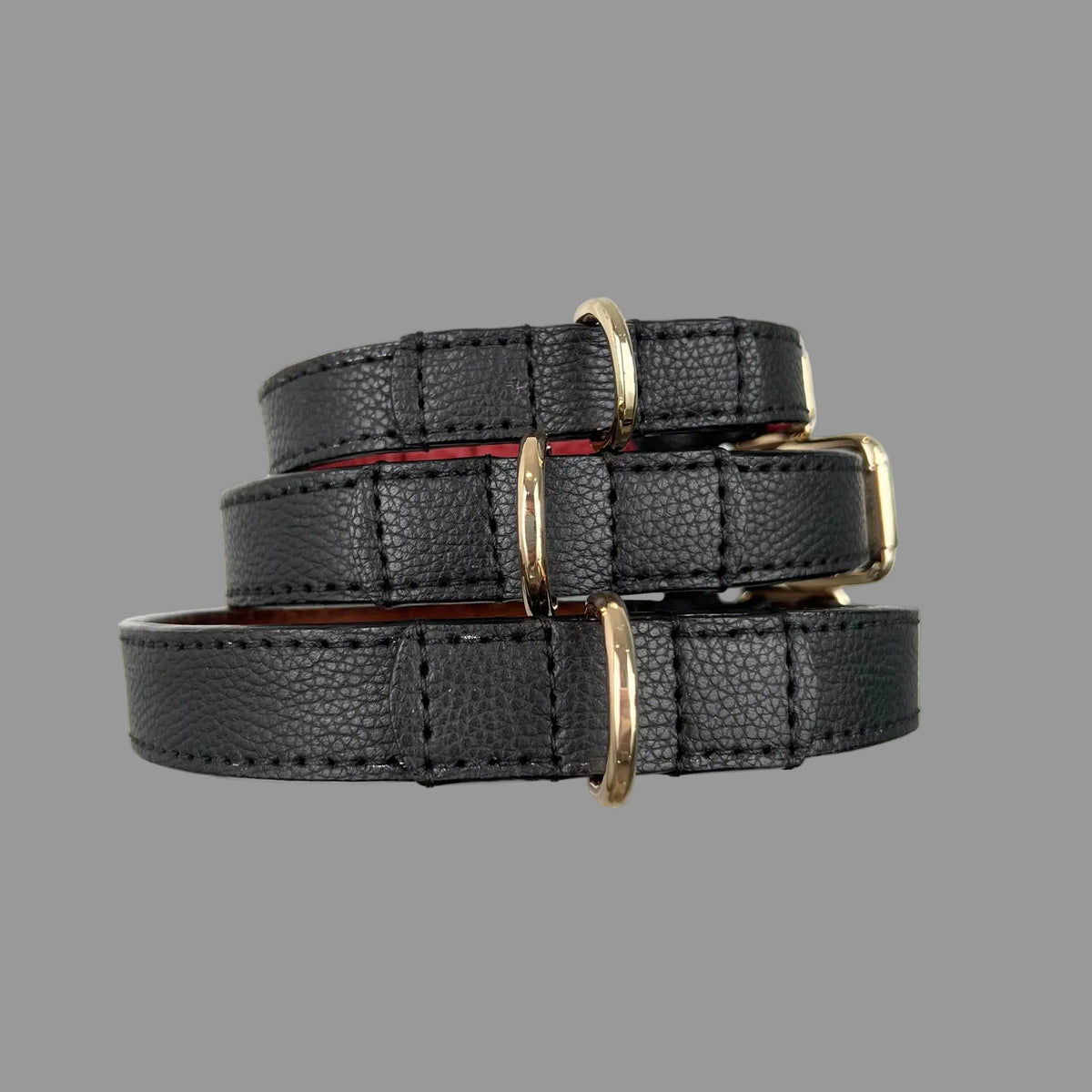 Stacked black pebbled leather dog collars showing gold-tone D-rings and reinforced, hand-stitched leather attachments.