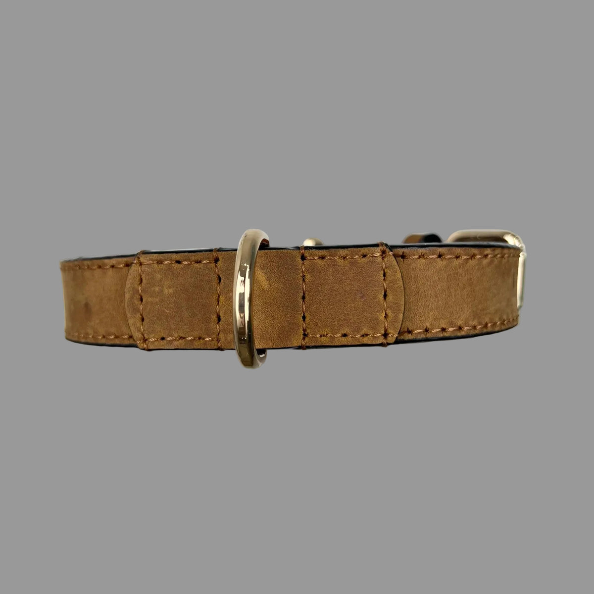 Close-up of a gold-tone D-ring secured by reinforced brown leather and hand-stitching on a dog collar.