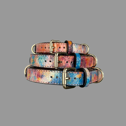 Three multicolour croc-embossed leather dog collars stacked to show gold-tone buckles and patterned keeper loops.