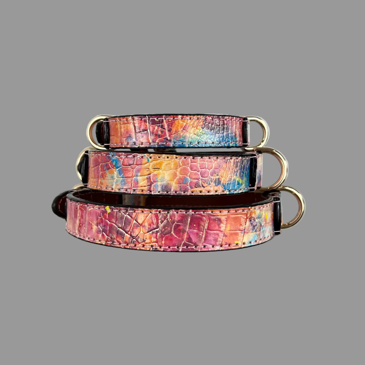 Three croc-embossed dog collars showing varied blue, pink and orange patterns, pale pink stitching and dark edges.