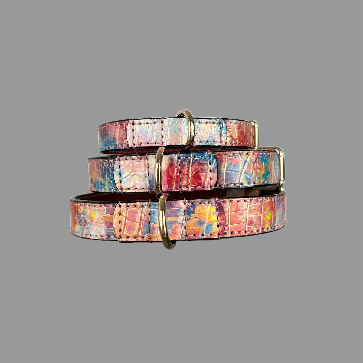 Stacked multicolour cowhide dog collars showing gold-tone D-rings and reinforced, hand-stitched leather attachments.