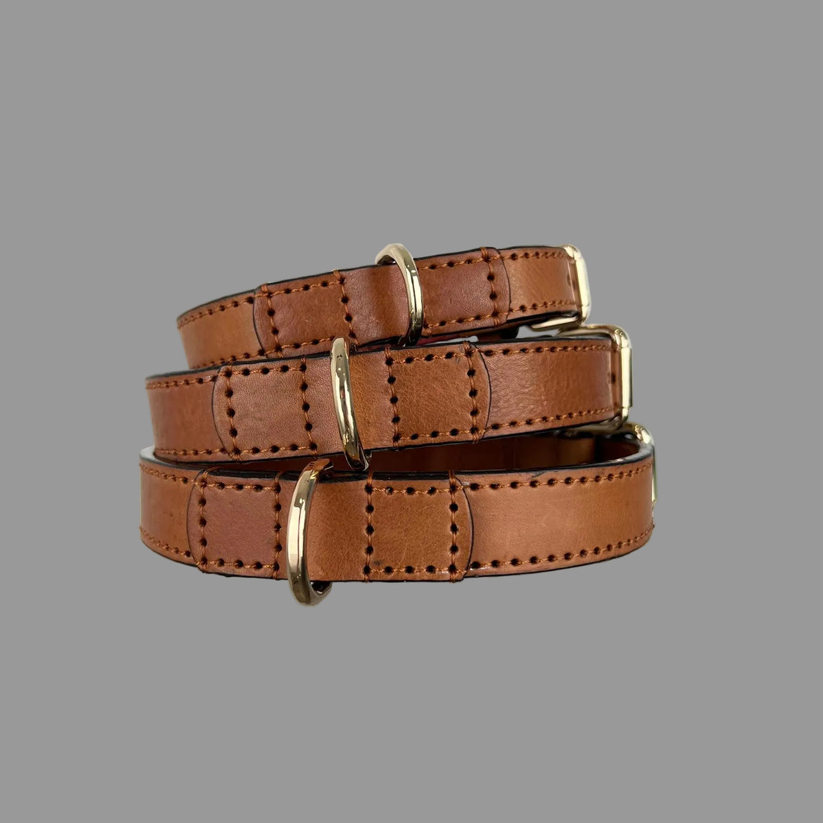 Three saddle brown collars showing gold-tone D-rings secured with hand-stitched leather reinforcement.
