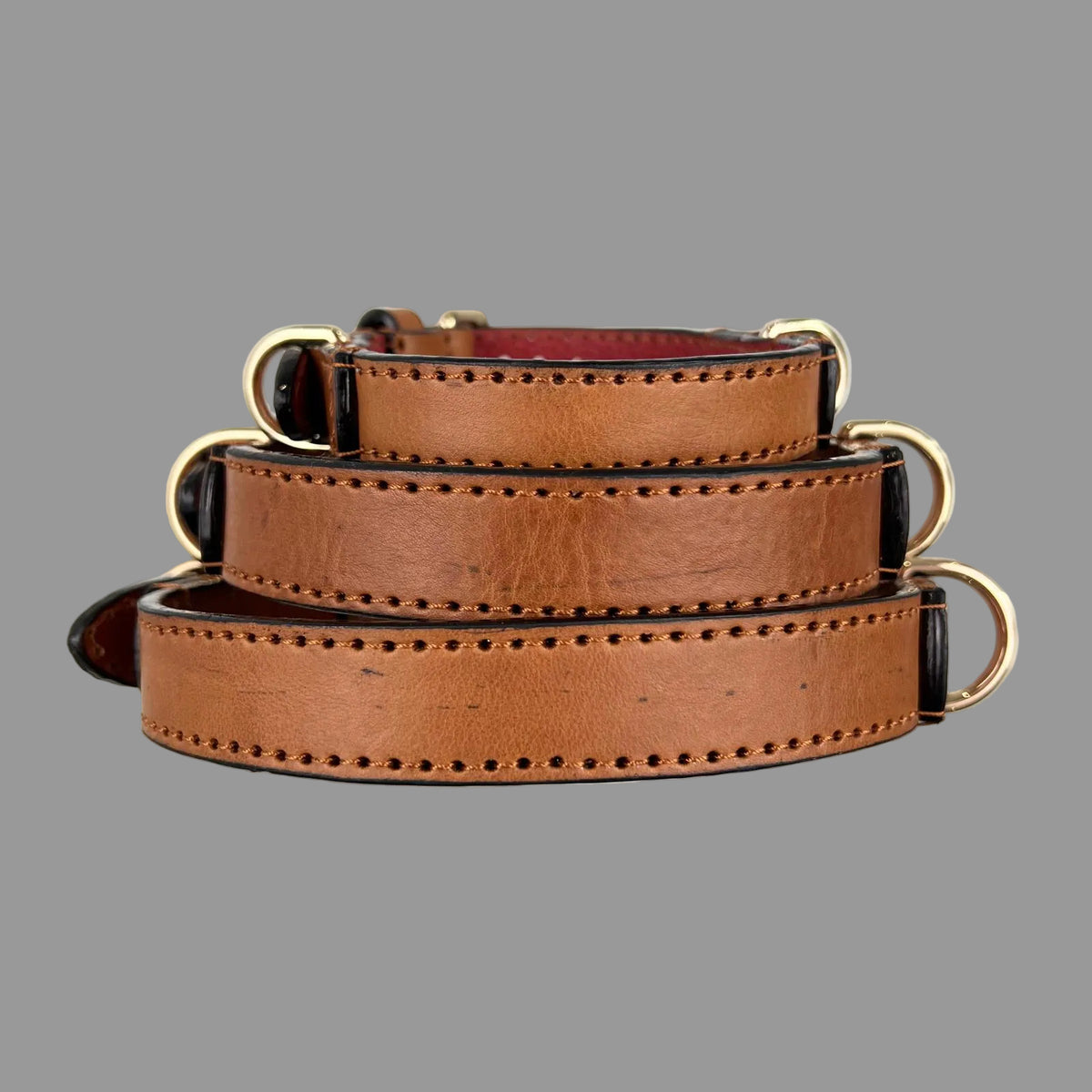 Three saddle brown leather dog collars stacked to show their strap widths, keepers and gold-tone fittings.