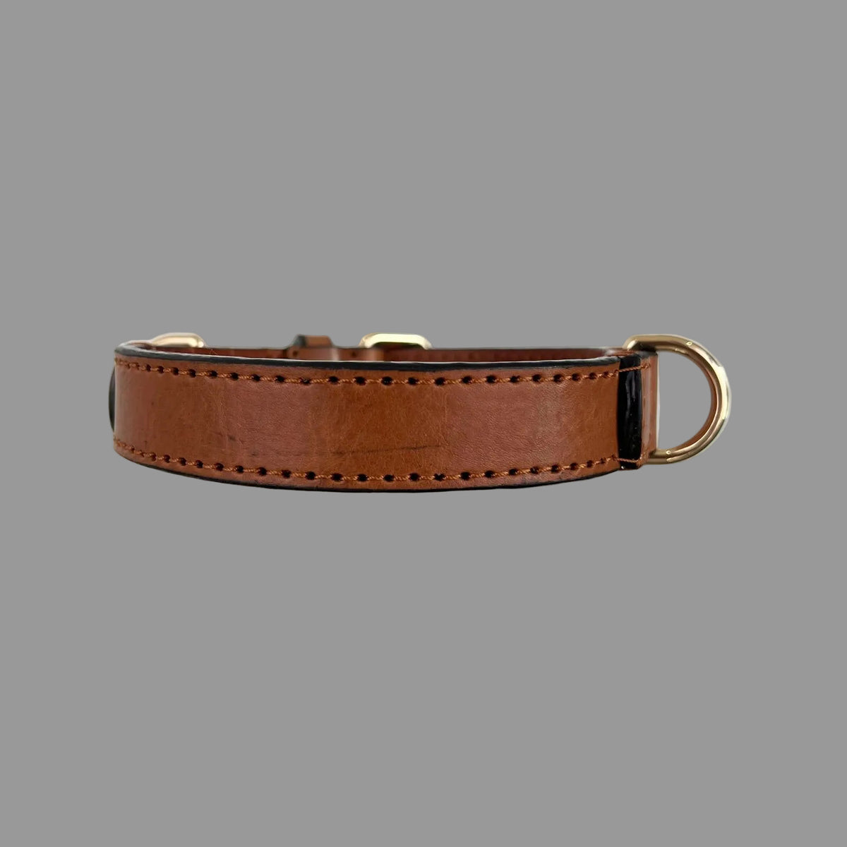Side view of a saddle brown cowhide dog collar showing natural grain, tonal hand stitching and a gold-tone D-ring.