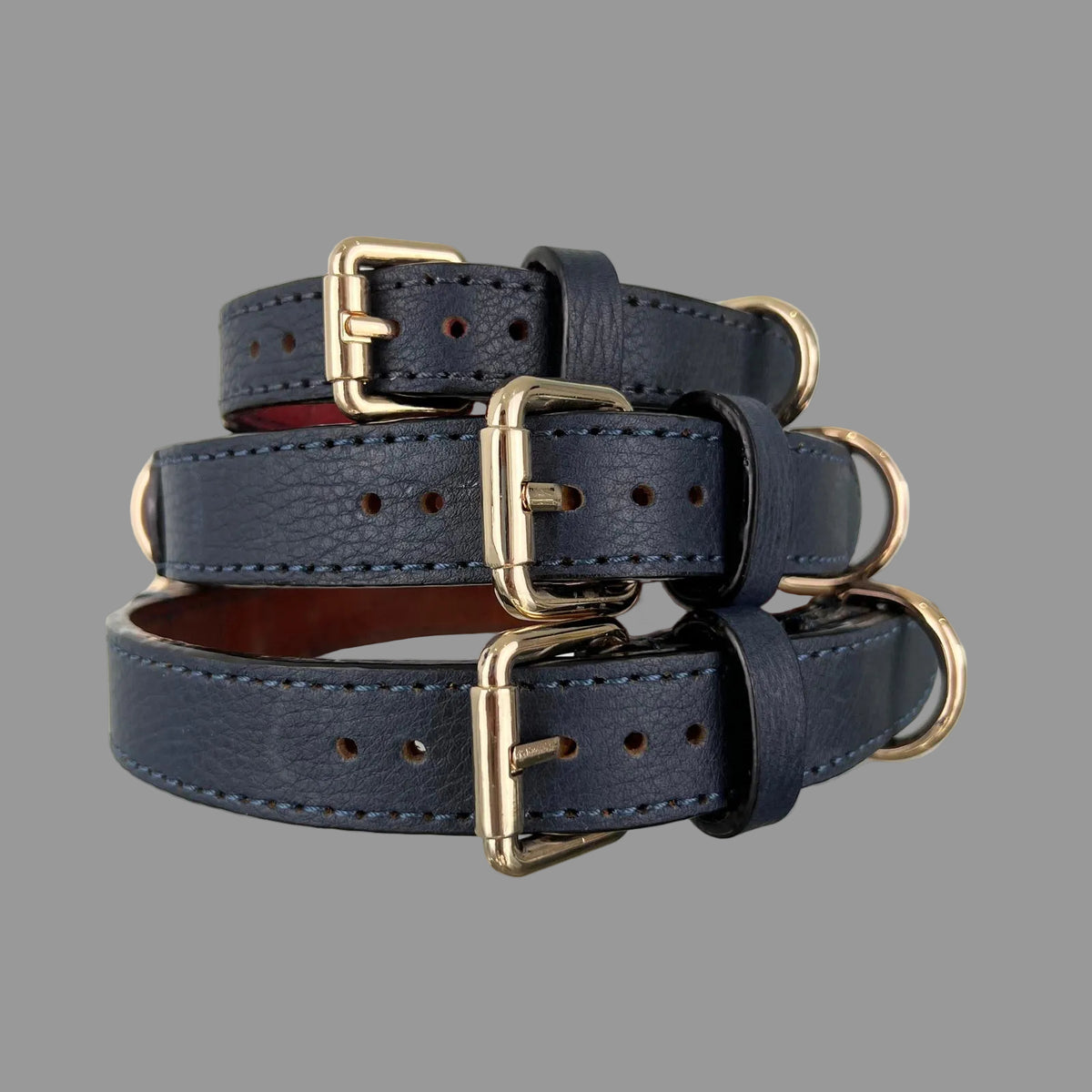 Stacked navy blue collars with gold-tone buckles and rounded strap ends; red lining is visible inside the smallest collar.