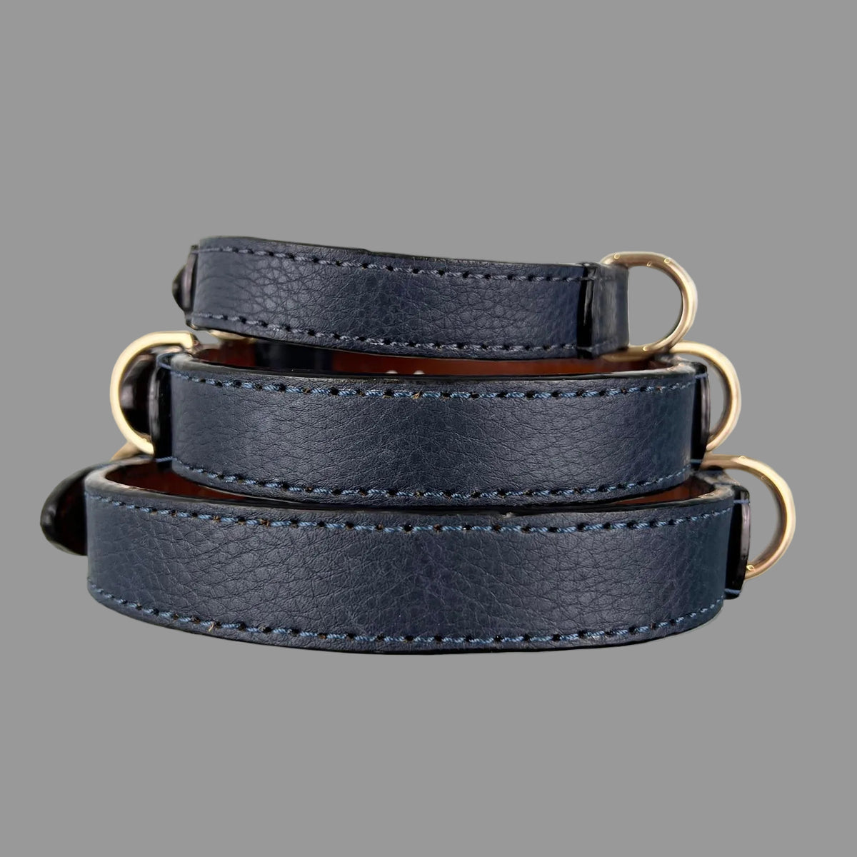 Three stacked navy blue dog collars showing the pebbled leather texture, tonal stitching and dark finished edges.