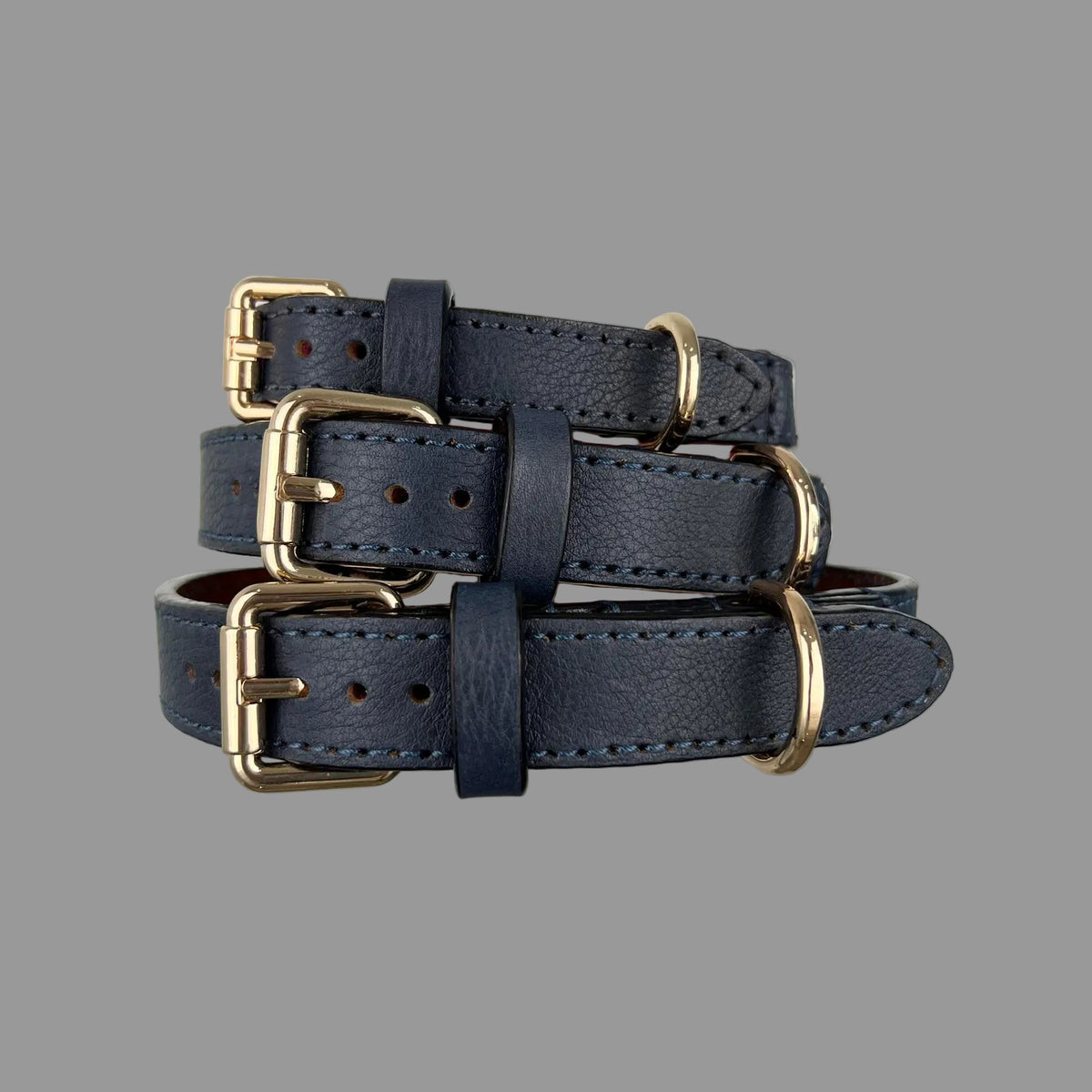 M, L and XL navy blue leather dog collars stacked to show gold-tone buckles, matching keepers and adjustment holes.