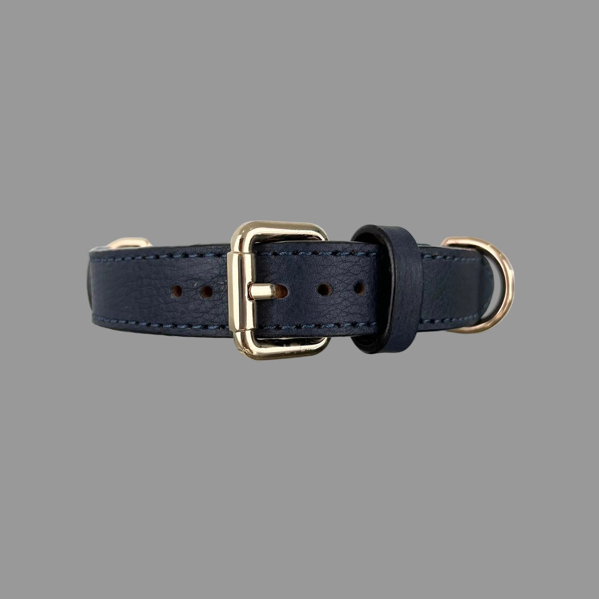 Close-up of a navy blue leather dog collar with a gold-tone buckle, adjustment holes and tonal hand stitching.