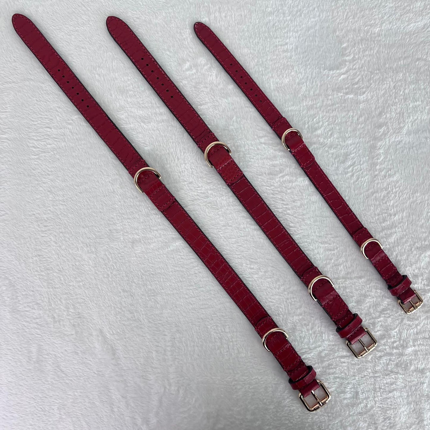 Three ruby red leather dog collars laid flat in sizes M, L and XL
