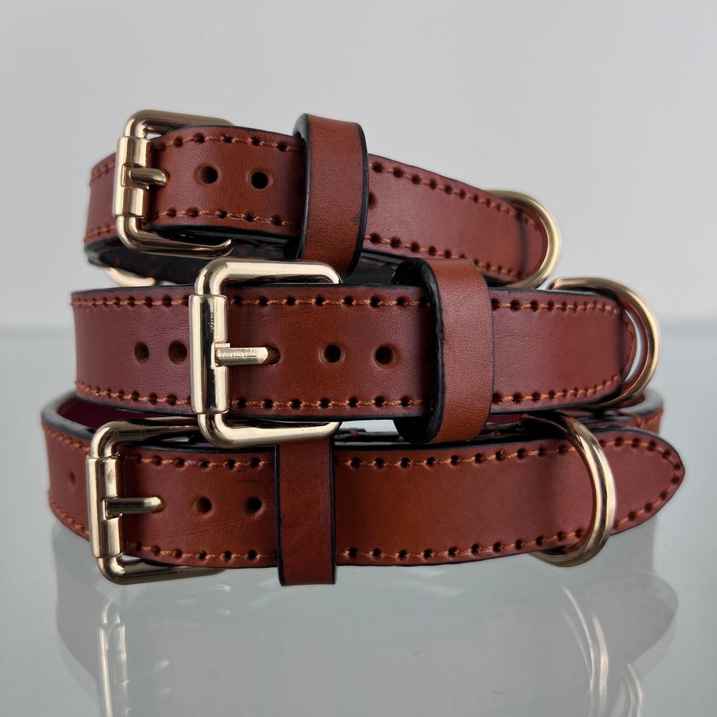 Three handmade cognac brown leather dog collars stacked in sizes M, L and XL