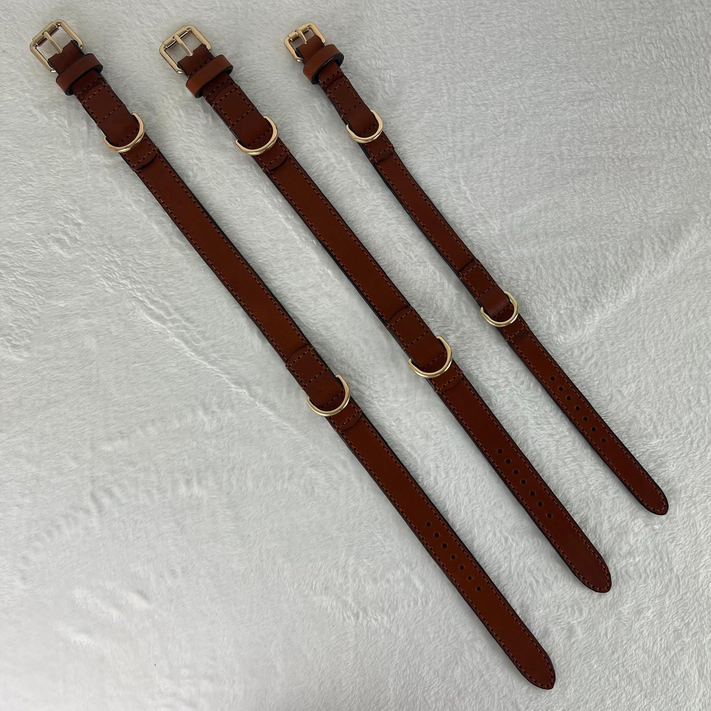 Cognac brown full-grain leather dog collars in sizes M, L and XL laid flat for size comparison